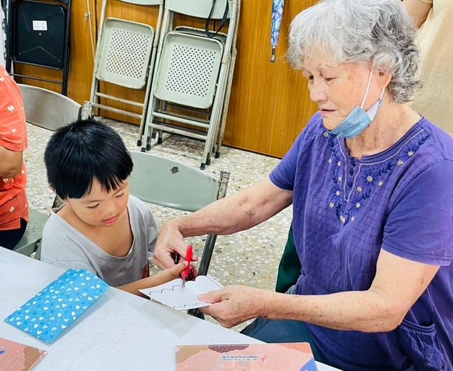 區長輩細心協助幼童使用剪刀製作圖樣,體現社區「老少共融」與互助共學的意涵。